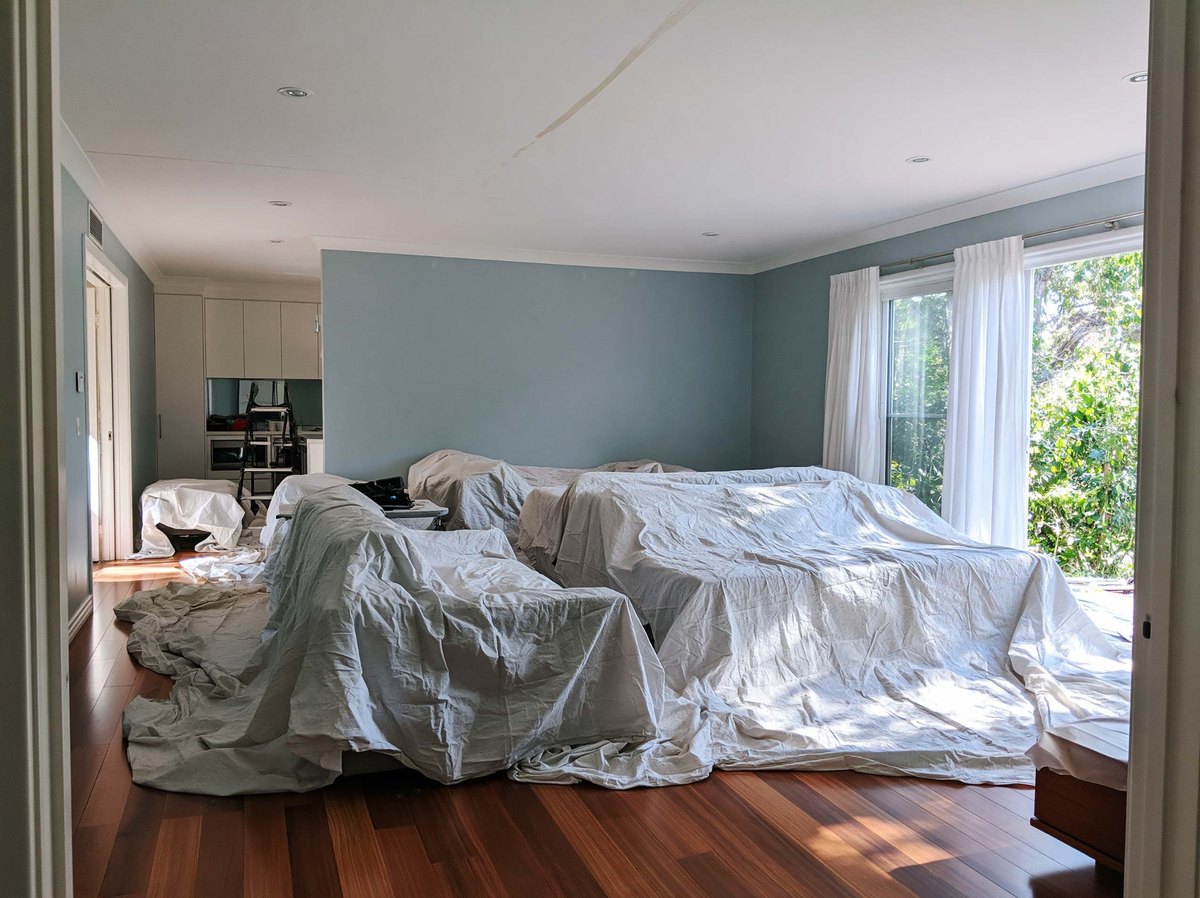 Living room furniture covered with protective sheets beneath a ceiling.