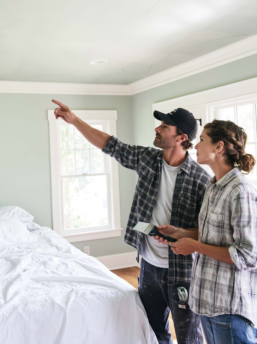 Two people looking at a ceiling above covered furniture.